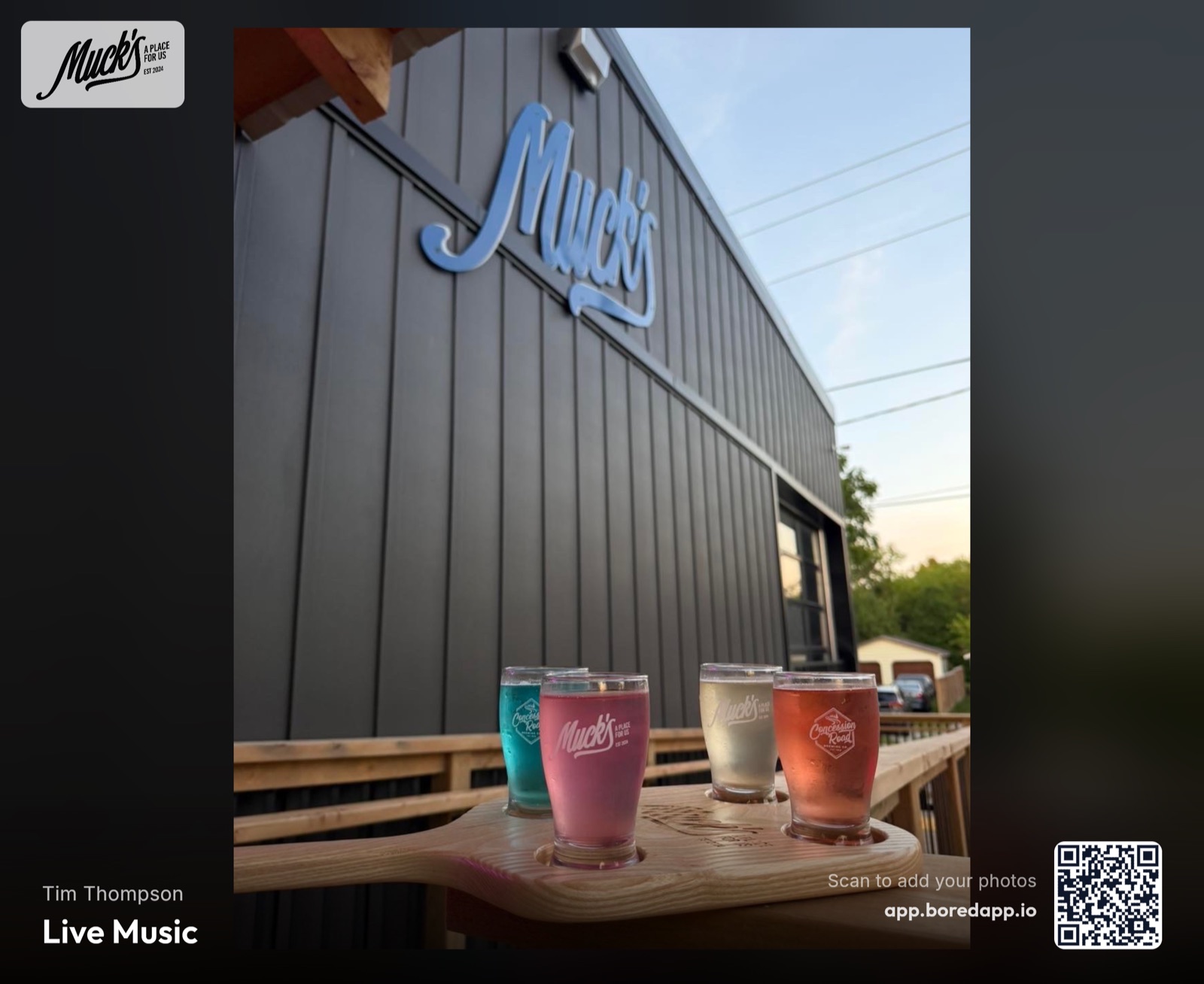 A BoredApp Photo Wall on a venue screen carrying the host's own branding — the Muck's logo in the corner, a guest's photo filling the frame, the event title and a join QR code along the bottom
