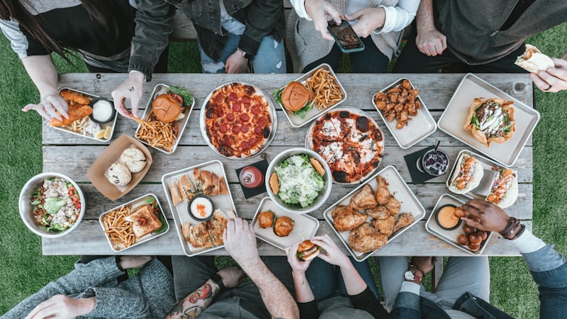 An overhead view of a long table covered in shared dishes, with hands reaching in